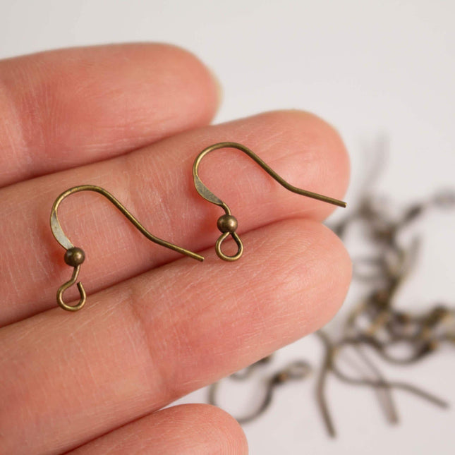 A hand holding a pair of brass earring hooks against a blurred background.