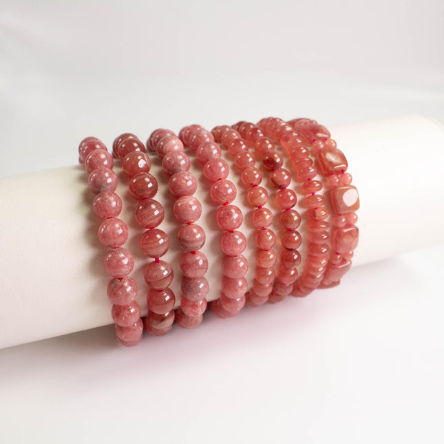 A collection of red beaded bracelets arranged in a row on a white surface.