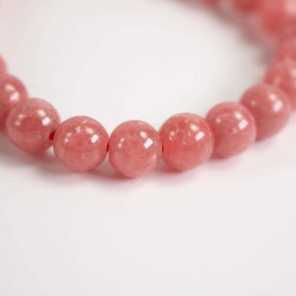 A close-up image of a bracelet made of small, round, pink beads arranged in a row.