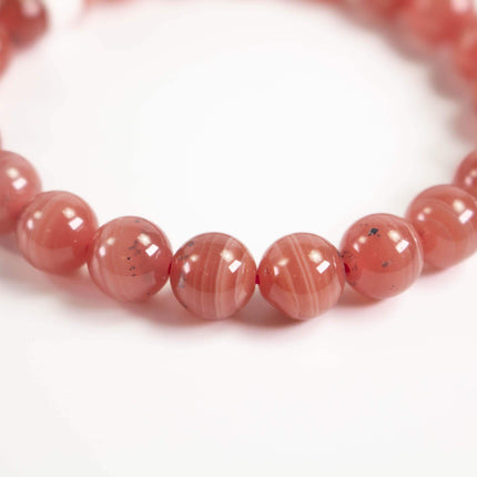 A close-up image of a bracelet composed of numerous round, pink beads arranged in a circular pattern.