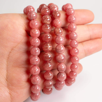 A hand holding a collection of pink beads, likely made of jade or similar material.