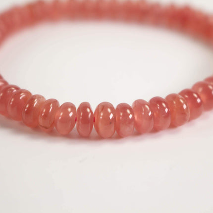 A close-up image of a bracelet made of small, round, pink beads arranged in a row.