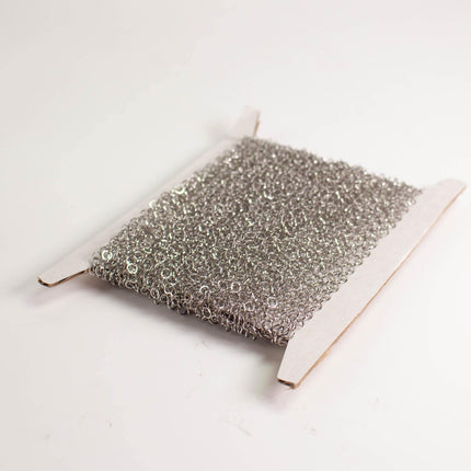 A piece of silver wire or metal mesh is shown in the image, resting on a white surface.