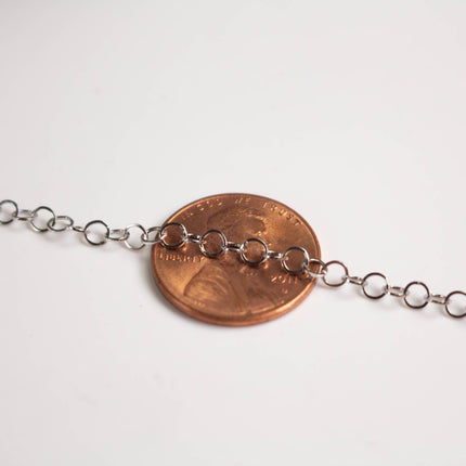 A close-up image of a chain of small silver links resting on top of a copper-colored penny.