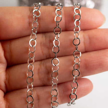 A close-up image of a person's hand holding a silver chain necklace with multiple silver rings.