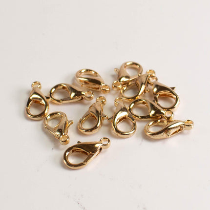 A group of gold-colored metal clasp hooks or lobster hooks arranged on a white background.